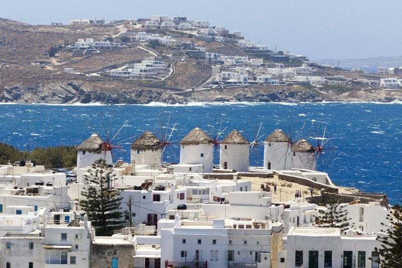 Iconic windmills overlook whitewashed houses and the sparkling blue sea in Mykonos, a famous Greek island loved by LGBTQ+ travelers.