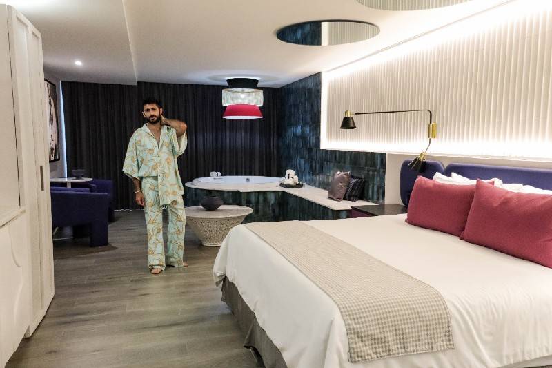  A modern hotel room with a king-sized bed, a man in a robe, and a jacuzzi in the corner.