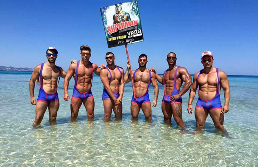 Group of muscular men posing in matching Superman swimsuits at a gay beach party in Ibiza.