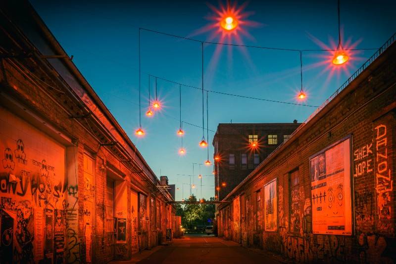 Beco coberto de grafite em Berlim, iluminado por luzes laranja penduradas ao entardecer.