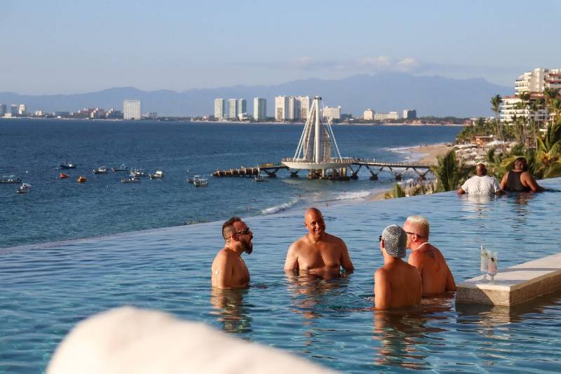 A group of men relaxing in an infinity pool with an ocean and city skyline view.