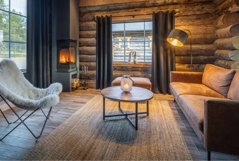 A rustic log cabin interior with a fireplace, fur chair, and warm lighting.