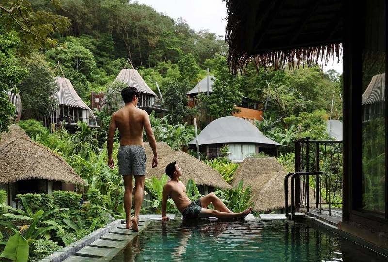 Two men at a private jungle pool with luxurious eco-lodges in the background.