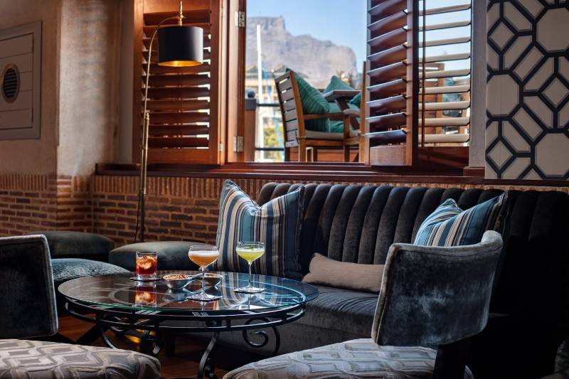 A cozy lounge with plush seating, cocktails on the table, and mountain views through an open window.