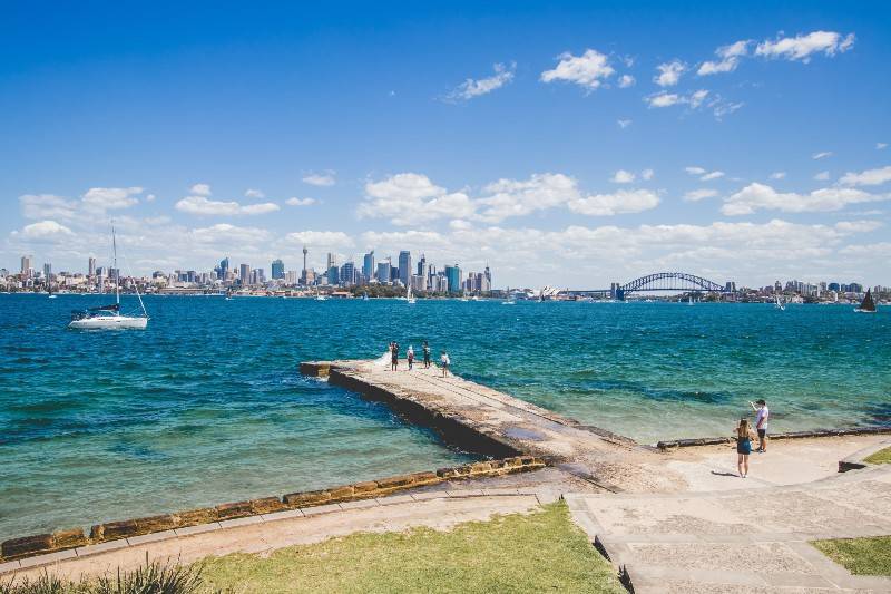 Porto de Sydney com horizonte, ponte e pessoas em um píer de pedra.
