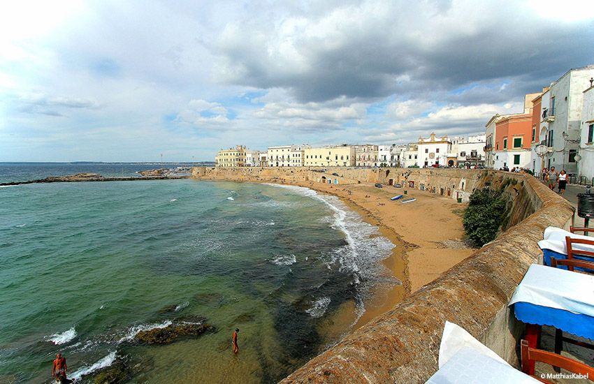Gallipoli’s old town beachfront with colorful buildings, calm sea, and a charming gay-friendly vibe.