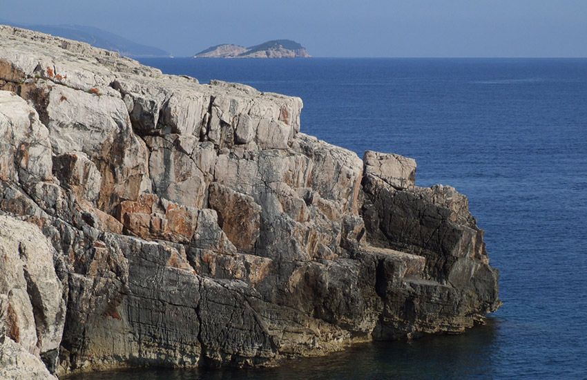 Steep rocky cliffs plunging into crystal-clear Adriatic Sea at Dubrovnik’s Lokrum gay naturist beach.