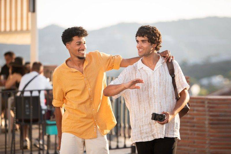 Two friends explore a lively rooftop bar in Torremolinos during golden hour, enjoying the vibrant gay-friendly atmosphere of the city.