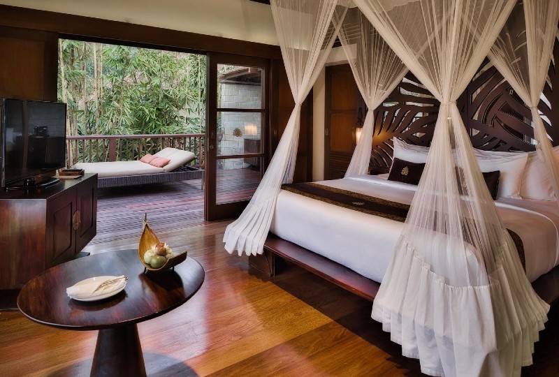 A curved infinity pool with lush greenery and a dining table on the deck.