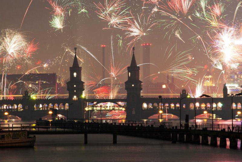 Fogos de artifício sobre uma ponte em Berlim com um céu nebuloso e luzes da cidade